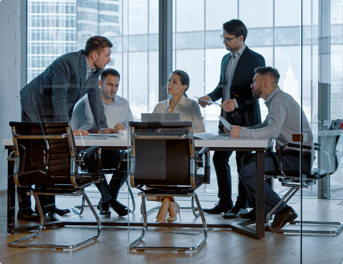 Image of people surrounding a table in a glass walled meeting room having a discussion