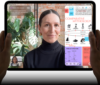 iPad Pro, front exterior, landscape orientation, space black colour rounded corners, black display bezel, hands holding left and right sides, display showing a FaceTime conversation being live translated, and an educational app showing a presentation of “Comparative Mythology” with text, diagrams and handwritten notes
