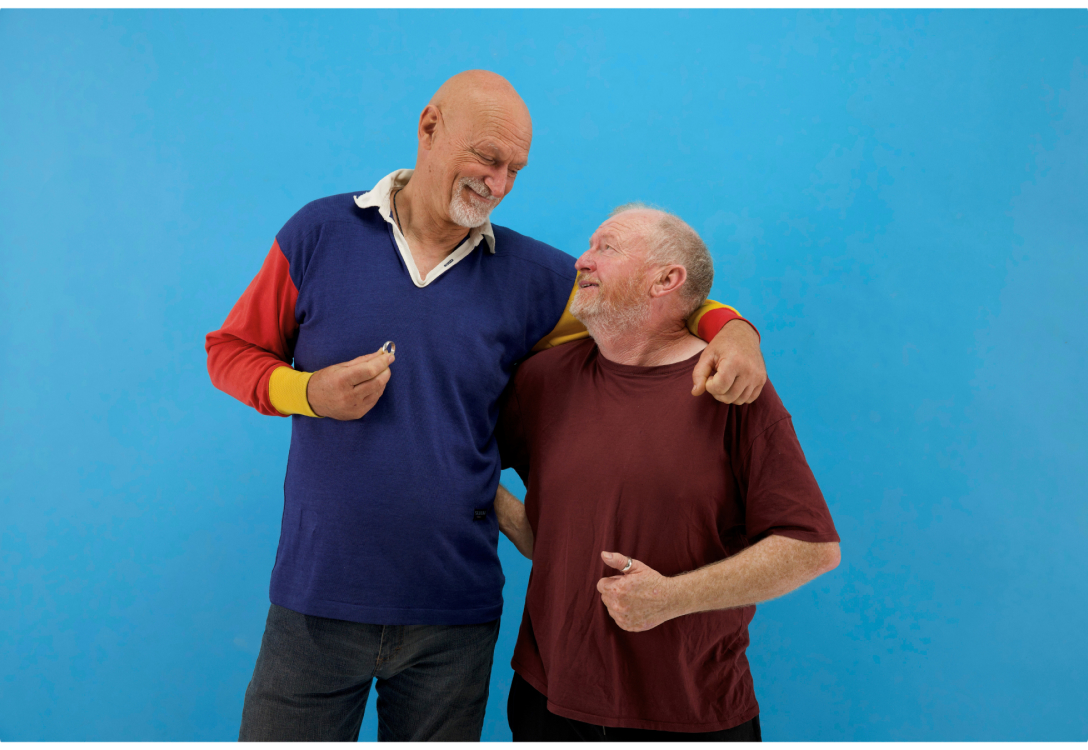 Photo of two men each holding onto a ring and looking at each other with their arm around the other