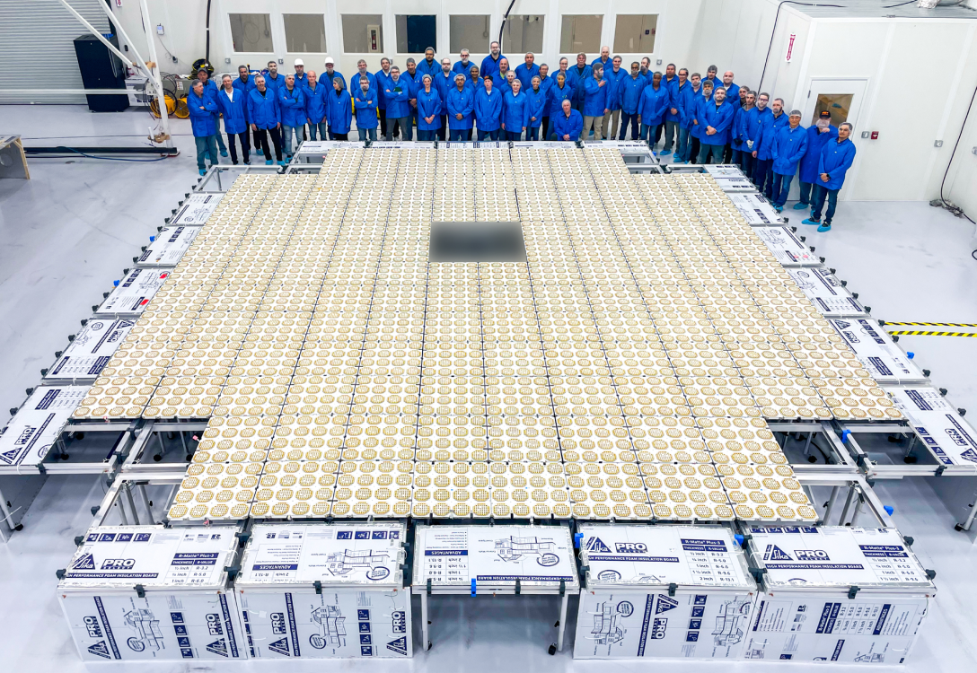 Image of a satellite on the ground with workers standing behind it