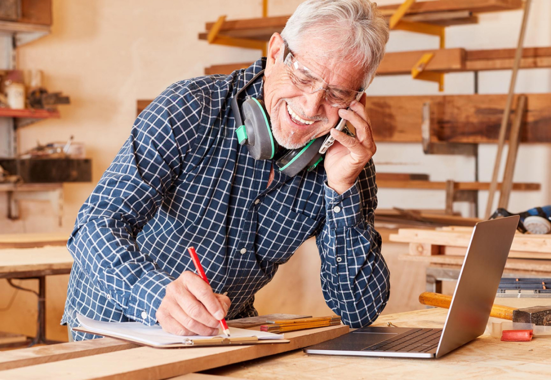 Man talking on the phone while writing something down leaning on a work bench