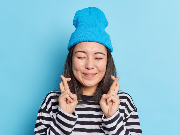 girl in blue beanie smiling with fingers crossed